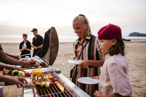 Mutter und Tochter stehen in der Nähe des Grills und halten Teller am Strand - MASF36608