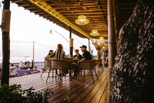 Familie genießt zusammen auf Stühlen sitzend auf der Veranda eines Restaurants im Urlaub - MASF36609