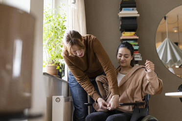 Krankenschwester hilft einer querschnittsgelähmten Frau, die zu Hause im Rollstuhl sitzt - MASF36623
