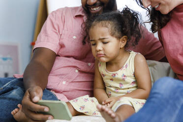 Cute girl looking at smart phone with parents at home - IKF00036