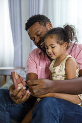 Father helping daughter in wearing shoes at home - IKF00040