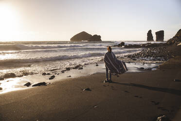 Junge Frau im Poncho steht am Strand - PCLF00360