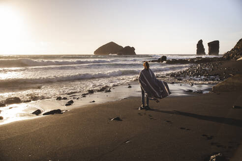 Young woman in poncho standing on shore at beach - PCLF00360