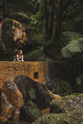 Junge Frau lehnt an einer Mauer im Wald - PCLF00368