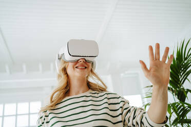 Happy woman playing games through VR glasses at home - MDOF00975