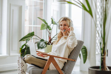 Happy freelancer with prosthetic legs sitting in chair at home - MDOF00996