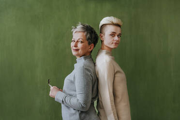 Selbstbewusste Frauen mit kurzen Haaren stehen an einer grünen Wand - YTF00701