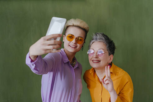 Fröhliche Damen, die einen Moment mit ihrem Smartphone festhalten und vor einer üppigen grünen Kulisse posieren - YTF00710