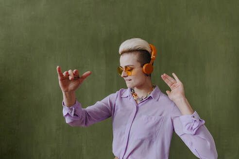 Unbeschwerte junge Frau mit drahtlosen Kopfhörern tanzt vor einer grünen Wand - YTF00720