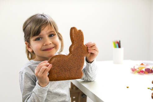 Smiling girl holding rabbit shaped cookie by table at home - MOMF01008