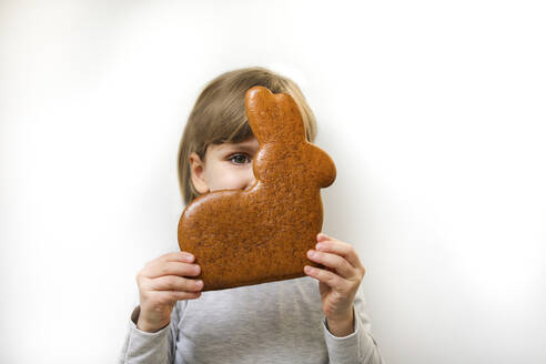 Girl with gingerbread Easter bunny covering face against white background - MOMF01009