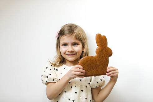 Lächelndes Mädchen hält Lebkuchen-Osterhase vor weißem Hintergrund - MOMF01010