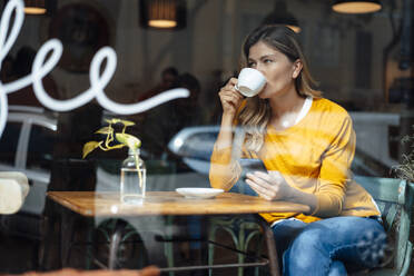 Frau mit Smartphone beim Kaffee trinken im Café durch Glas gesehen - JOSEF18251