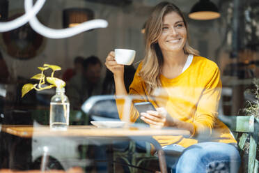 Glückliche Frau mit Kaffeetasse im Café durch Glas gesehen - JOSEF18252