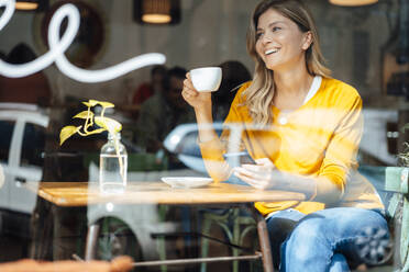 Glückliche Frau mit Mobiltelefon und Kaffeetasse am Tisch im Café - JOSEF18253