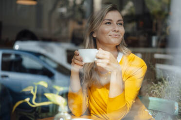 Nachdenkliche Frau mit Kaffeetasse schaut durch das Fenster - JOSEF18256