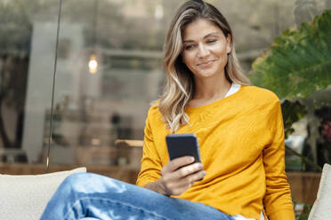 Lächelnde Frau mit Smartphone in einem Café sitzend - JOSEF18266