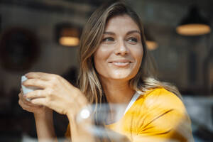 Lächelnde Frau mit Kaffeetasse im Café durch Glas gesehen - JOSEF18267