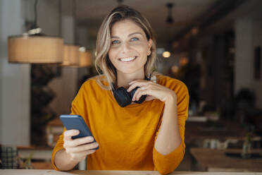 Glückliche Frau mit Smartphone im Café sitzend - JOSEF18271