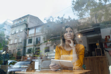 Kontemplative Frau mit Tablet-PC in einem Café, gesehen durch ein Glas mit Spiegelung - JOSEF18276