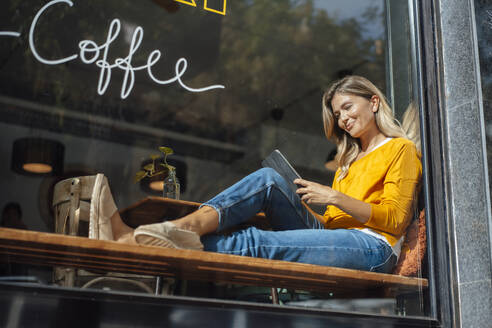 Lächelnde Frau, die in einem Café einen Tablet-PC benutzt, gesehen durch Glas - JOSEF18296