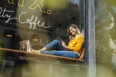 Glückliche Frau mit Tablet-PC am Fenster eines Cafés - JOSEF18297