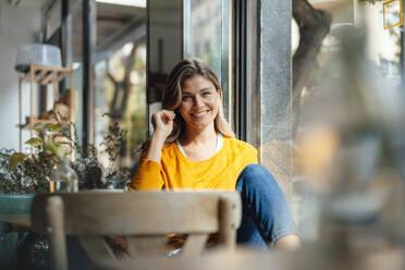 Happy woman sitting by window in cafe - JOSEF18301