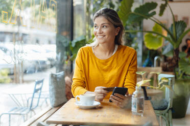 Glückliche Frau mit Kreditkarte und Mobiltelefon in einem Café sitzend - JOSEF18309