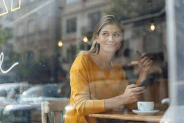 Lächelnde Frau mit Kreditkarte und Smartphone im Cafe sitzend - JOSEF18313