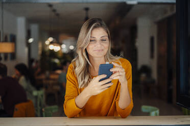 Lächelnde Frau mit Bond-Haar, die ein Smartphone in einem Café benutzt - JOSEF18318