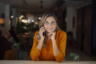 Lächelnde Frau, die in einem Café durch ihr Smartphone schaut - JOSEF18319