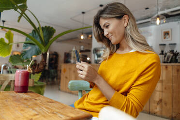 Lächelnde Frau, die mit ihrem Smartphone in einem Café einen Saft fotografiert - JOSEF18338