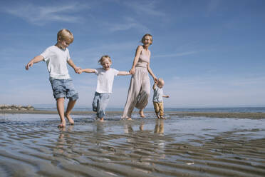 Happy mother holding hands with children and enjoying at beach - NDEF00486