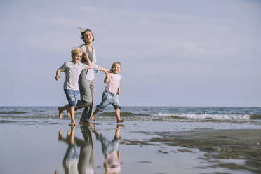 Happy mother running with daughter and son on shore at beach - NDEF00497
