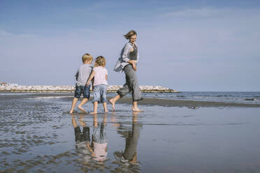 Happy mother playing with daughter and son on shore at beach - NDEF00498