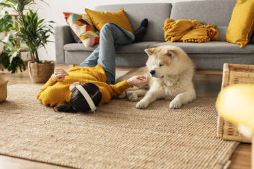 Woman wearing wireless headphones listening to music and stroking dog at home - JCCMF10129