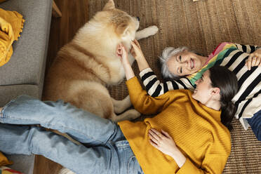 Glückliche Mutter und Tochter streicheln den Hund, der zu Hause auf dem Teppich liegt - JCCMF10132