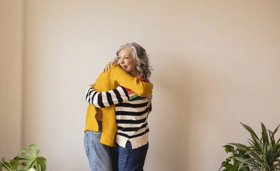 Glückliche Mutter umarmt Tochter vor der Wand zu Hause - JCCMF10152