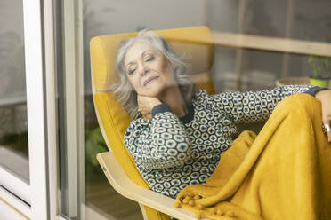 Smiling mature woman resting in chair seen through glass window - JCCMF10161