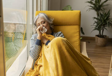 Reife Frau mit Taschentuch, die sich am Fenster zu Hause die Nase putzt - JCCMF10163