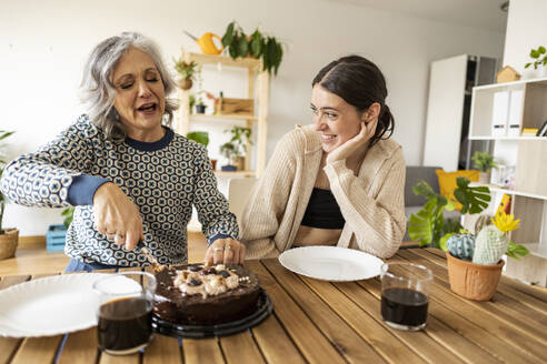 Mother cutting cake with daughter sitting at table - JCCMF10174