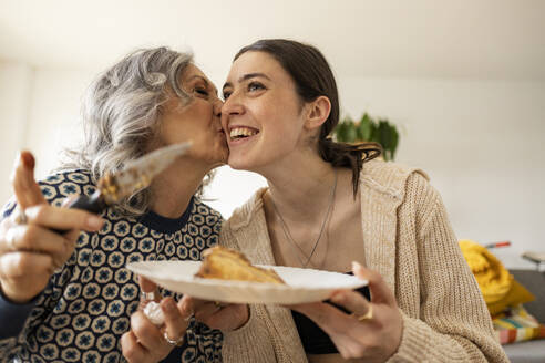 Mother serving cake and kissing daughter at home - JCCMF10175