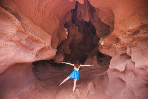 Young woman standing on one leg with arms outstretched in cave - PCLF00397