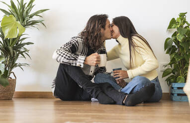 Romantisches Paar hält Kaffeetassen und küsst sich im neuen Zuhause - JCCMF10188
