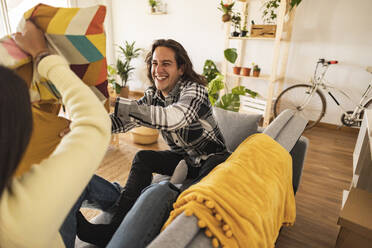 Happy couple playing pillow fight with each other at new home - JCCMF10194