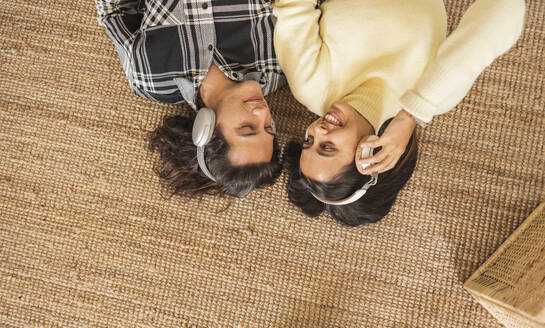 Glückliche Frau mit Freund und Kopfhörern auf dem Teppich zu Hause liegend - JCCMF10200