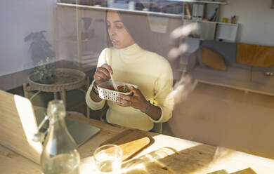 Freiberufler isst Snack mit Laptop auf dem Tisch im Heimbüro - JCCMF10208
