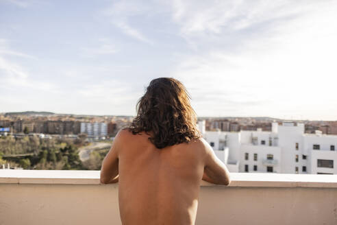 Hemdloser junger Mann mit langen Haaren auf einem Balkon stehend - JCCMF10237
