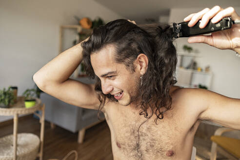 Happy man cutting hair with electric razor at home - JCCMF10240