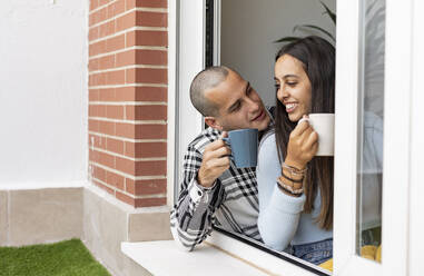 Happy couple having coffee near window at home - JCCMF10248